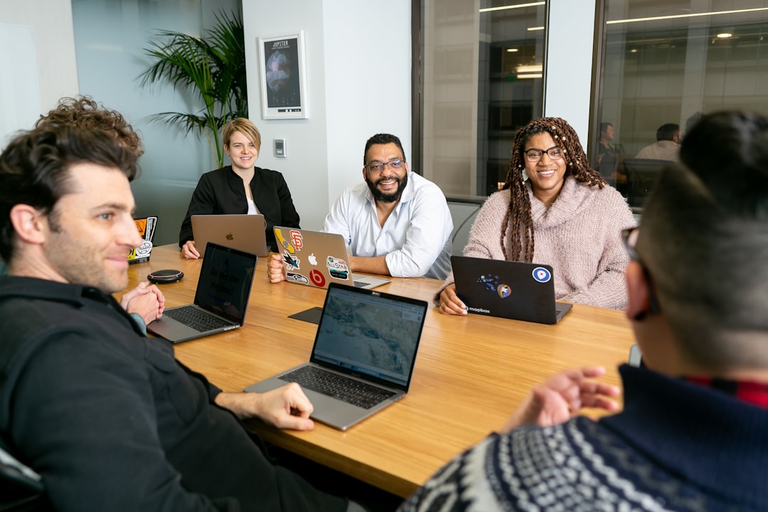 seo vs geo — four people all on laptops, two men and two women, listen to person talking in a board meeting